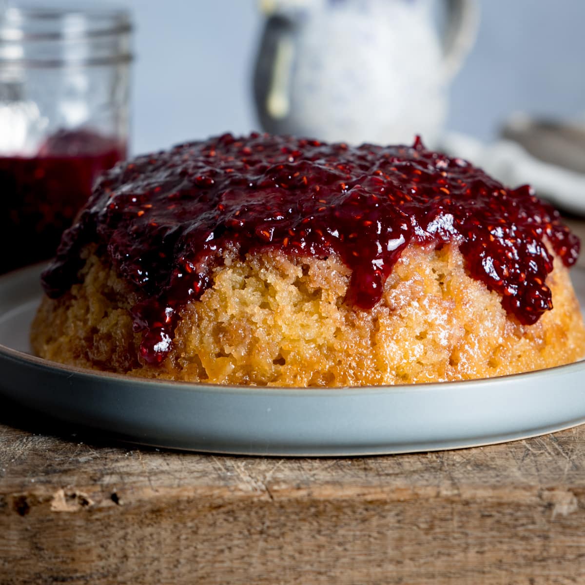 a slow cooker steamed jam sponge cake on a grey plate sat on a wooden chopping board.