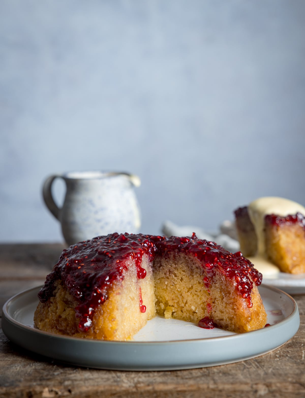 A sliced open steamed jam sponge cake on a grey plate with the jam dripping down the side.