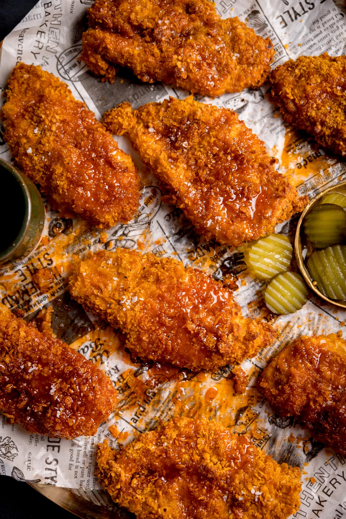 Overhead image of crispy baked chicken breast fillets on a baking tray with sliced pickles. The chicken has been drizzled with hot honey sauce.