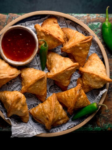 Overhead picture of a plate full of handmade Indian style Samosas on a rustic wooden board.