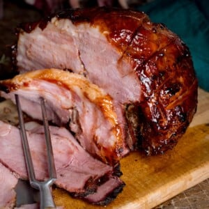 Sliced slow cooker gammon on a wooden board with a carving fork.