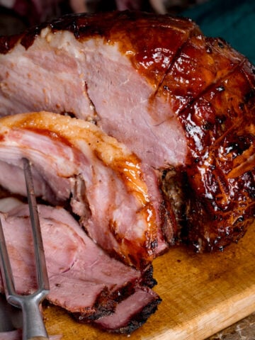 Sliced slow cooker gammon on a wooden board with a carving fork.