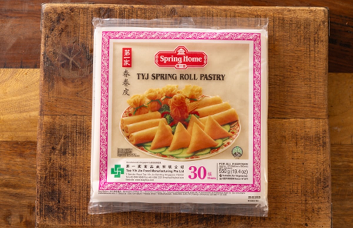 Picture of spring roll pastry in its package sat on a wooden chopping board.
