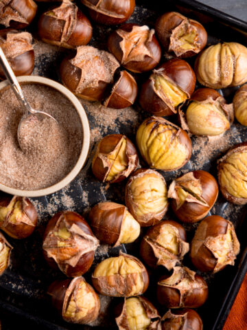Roasted Chestnuts on a baking tray with a bowl of cinnamon sugar.