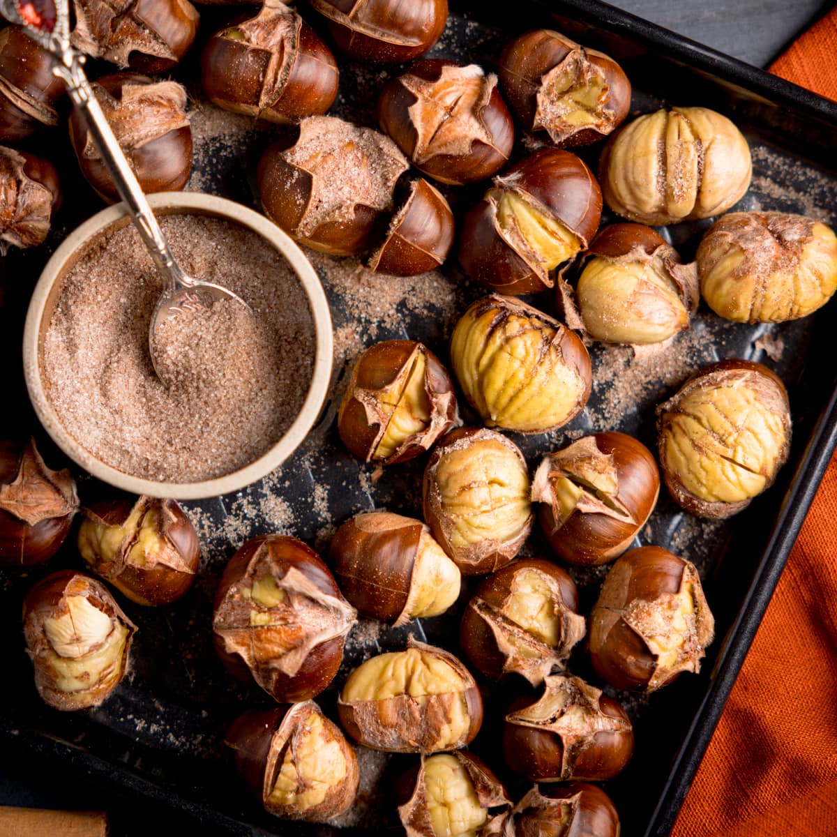 Roasted Chestnuts on a baking tray with a bowl of cinnamon sugar.