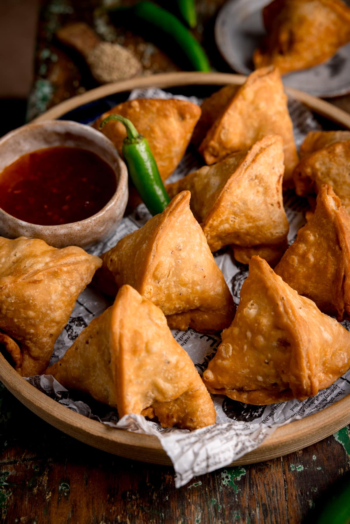 Close up picture of some homemade samosa's on a stone plate with a little dish of sweet chilli sauce on the side.