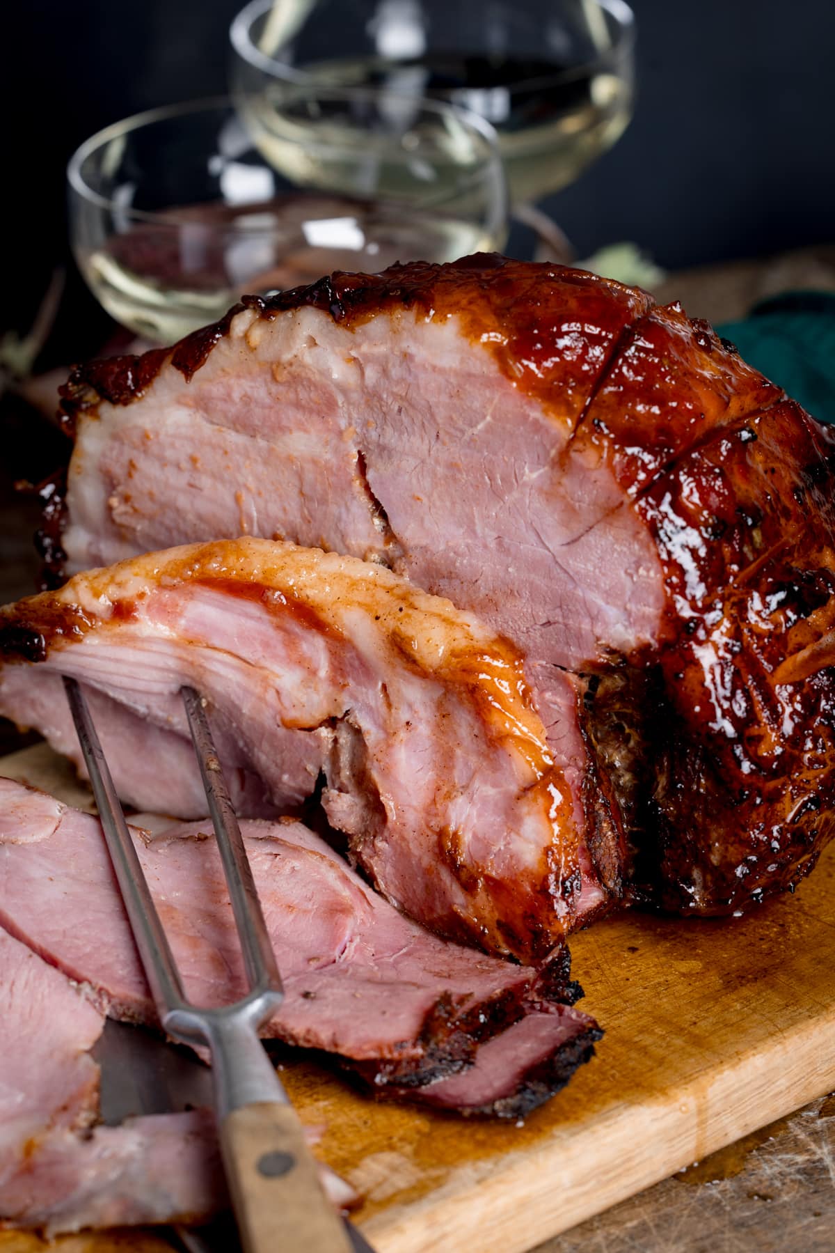 Close up pictures of a slow cooker gammon joint with some slices sliced off and carving fork in the foreground.