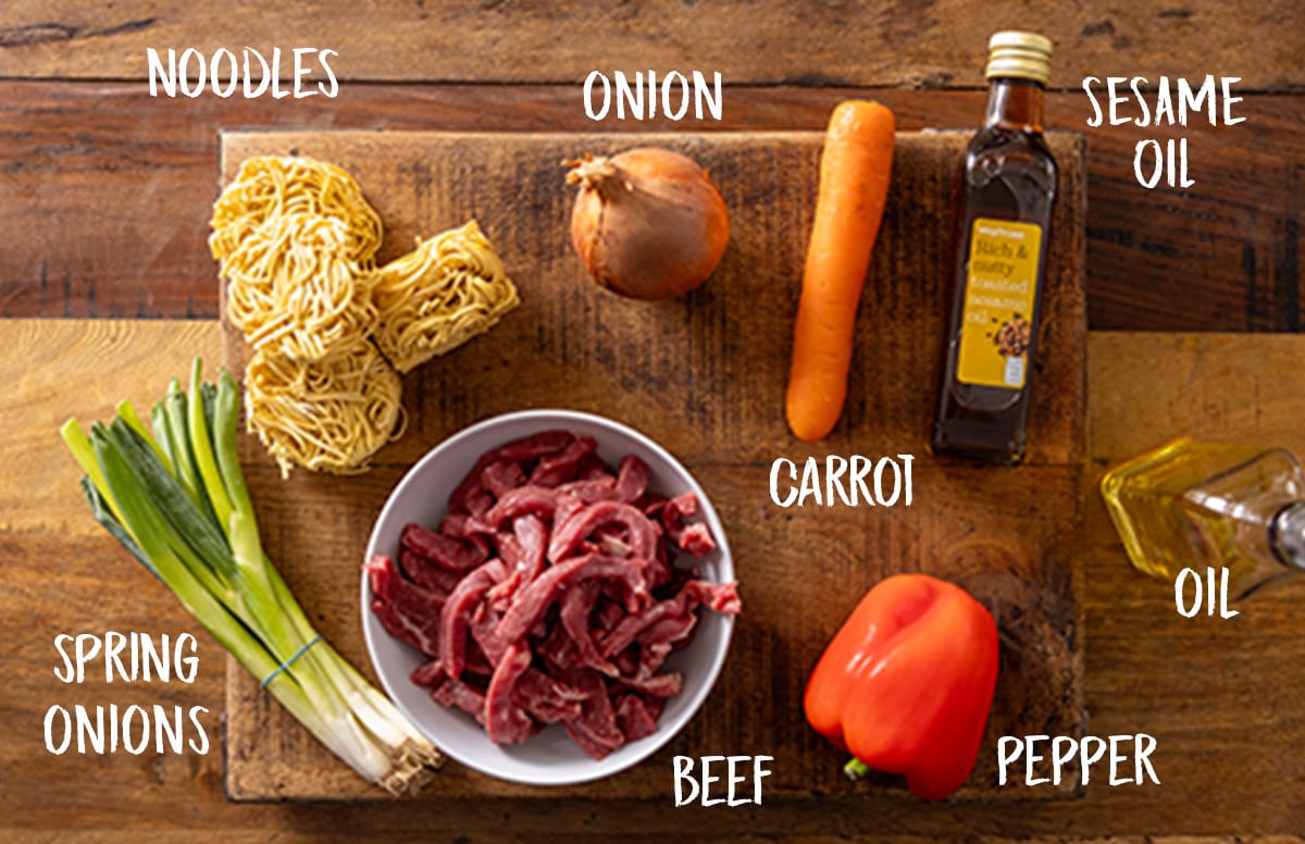 Ingredients for a beef noodle stir fry on a wooden board.