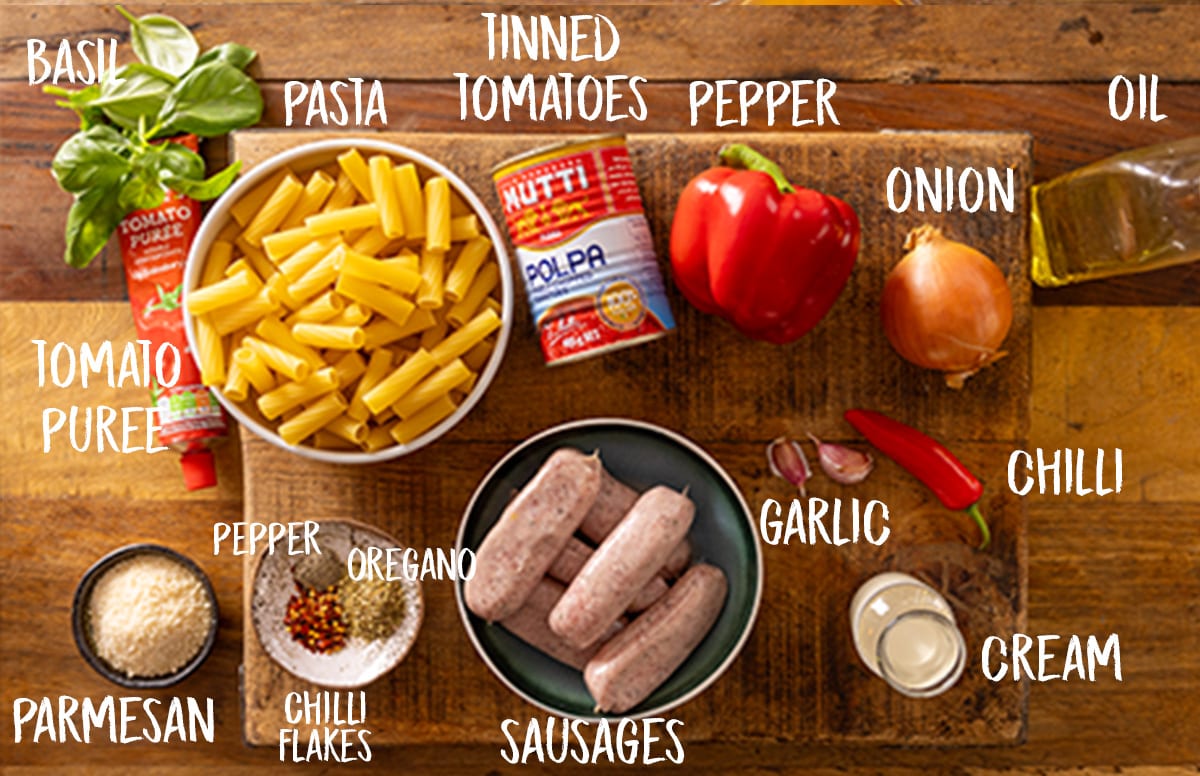 Ingredients for spicy sausage rigatoni on a wooden board.