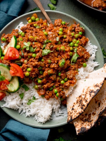 Overhead picture of a bowl full of Keema Curry sat on a bed of boiled basmati rice with a toasted chapati folded and wedged in the side of the dish.