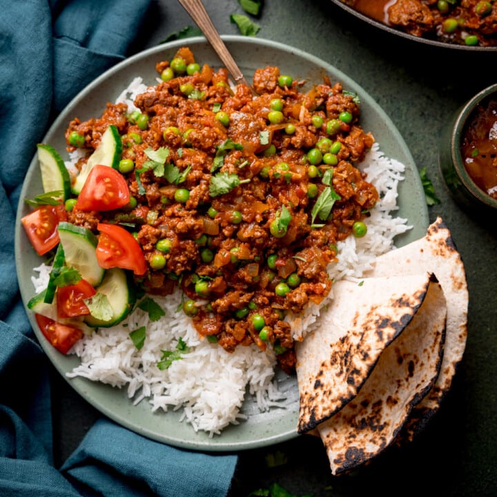 Overhead picture of a bowl full of Keema Curry sat on a bed of boiled basmati rice with a toasted chapati folded and wedged in the side of the dish.