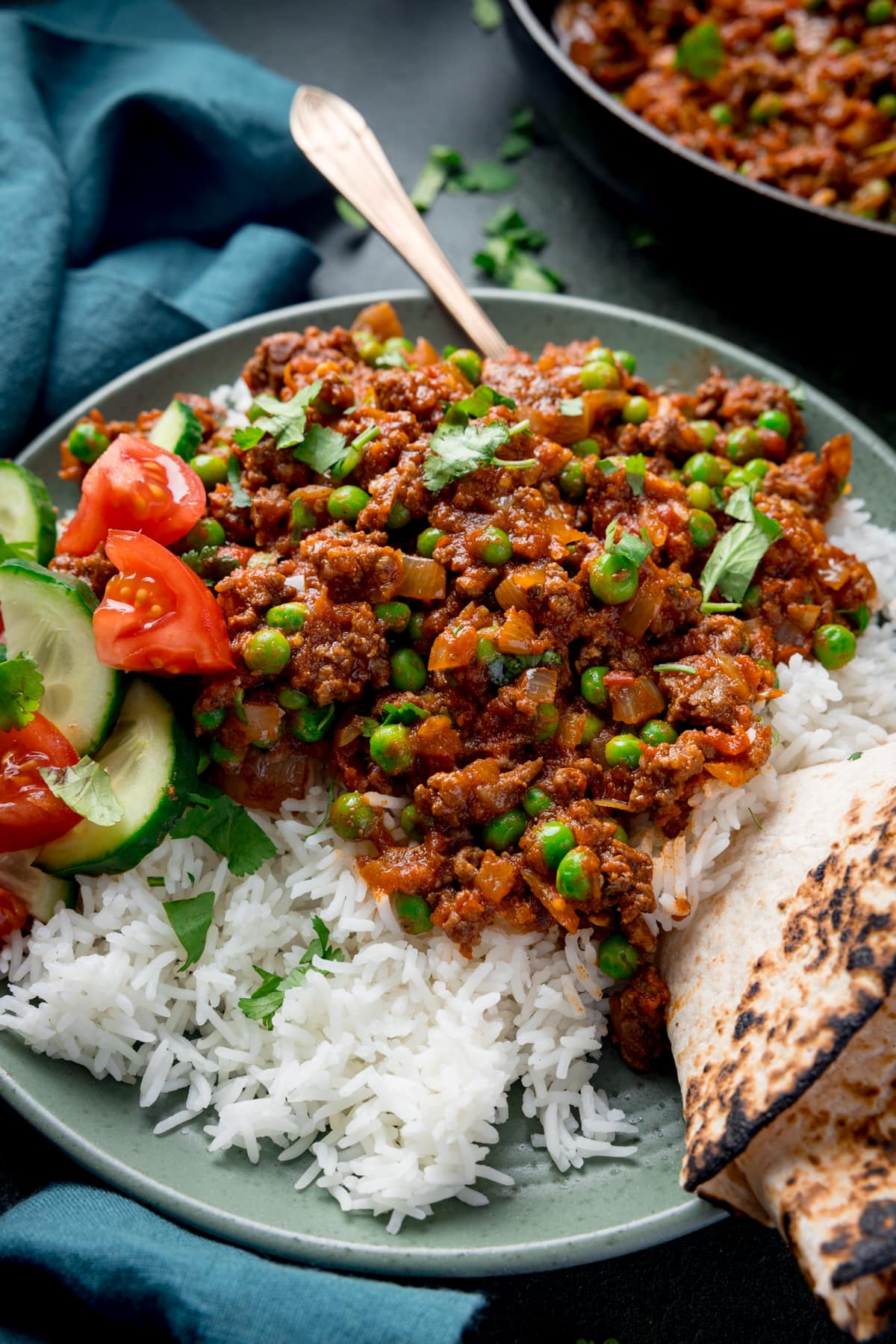 Close up picture of a bowl full of Keema Curry sat on a bed of boiled rice rice with a toasted chapati folded and wedged in the side of the dish.