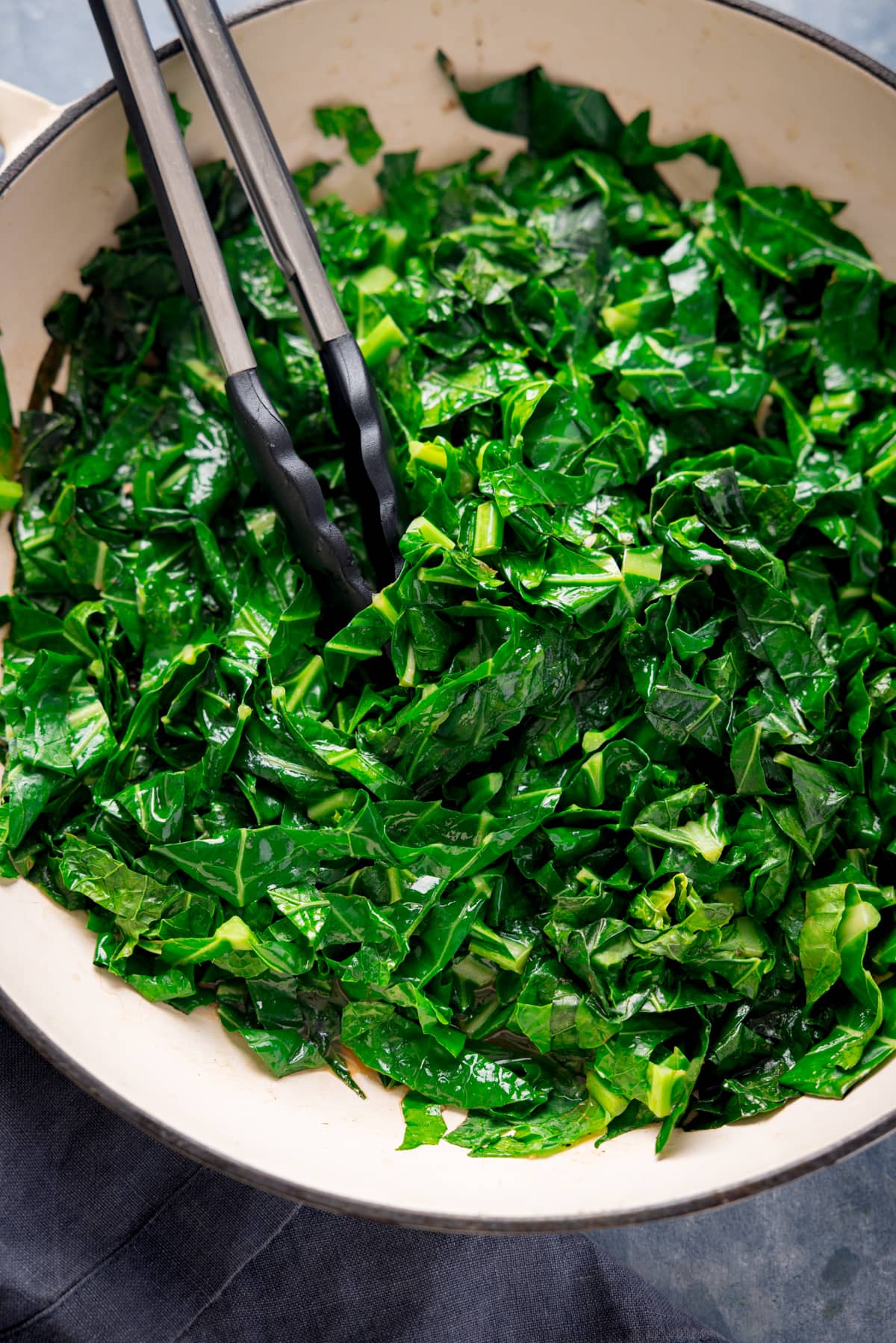 Overhead image of pan fried spring greens in a white pan. There is a set of tongs nestled in the spring greens.