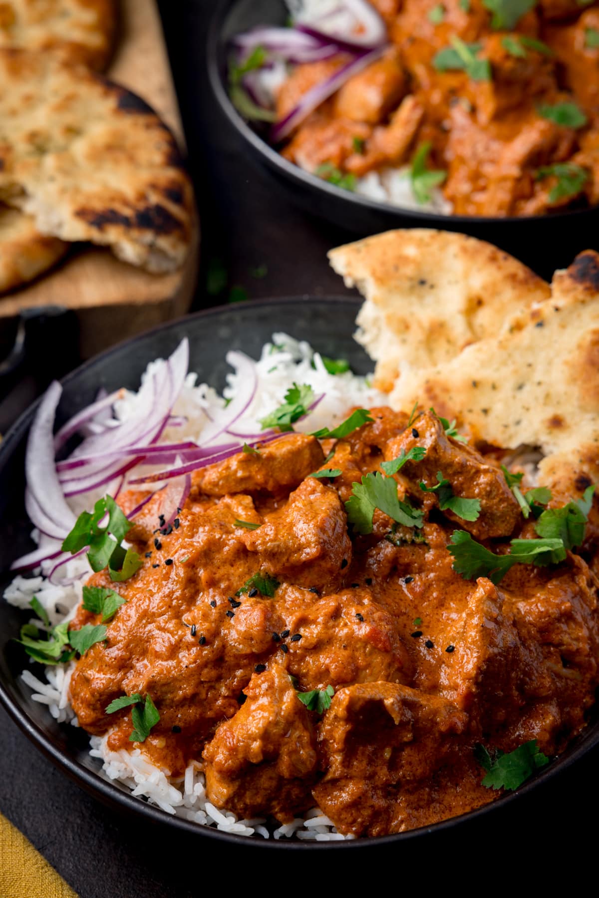 A bowl full of boiled rice and crock pot butter chicken with some sliced red onion and naan bread in the corner of the bowl.
