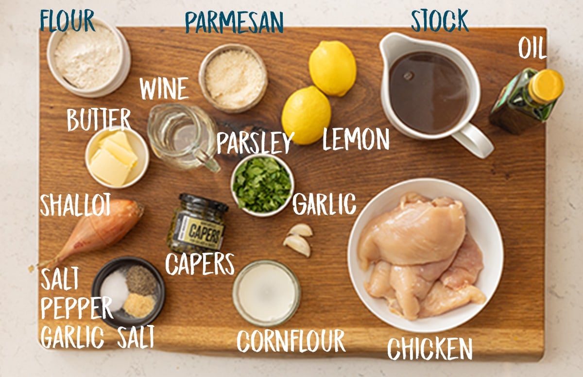 Ingredients for lemon chicken piccata on a wooden board.
There is a text ovelay showing the ingredient names.