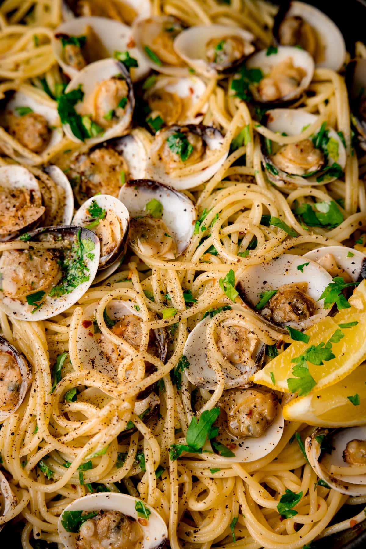 Close up overhead image of Spaghetti Vongole (spaghetti with clams) topped with parsley and lemon wedges.