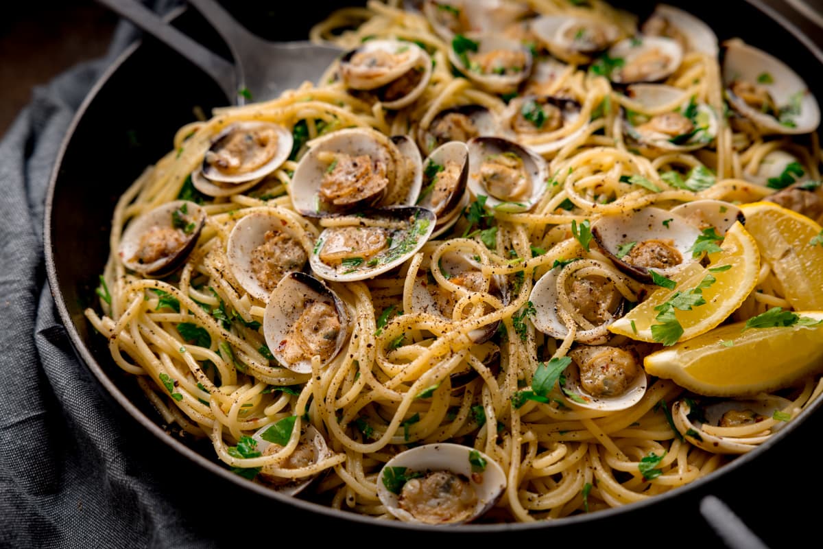 A pan of spaghetti and open clams sprinkled with chopped parsley.