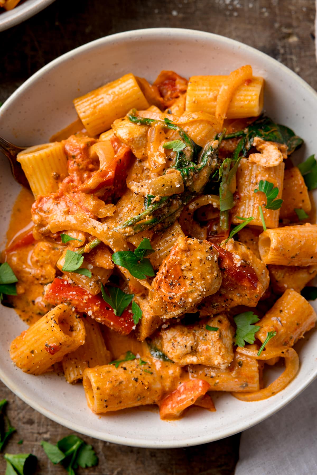 A close-up overhead image of a white bowl filled with Tuscan Chicken Pasta on a wooden background.