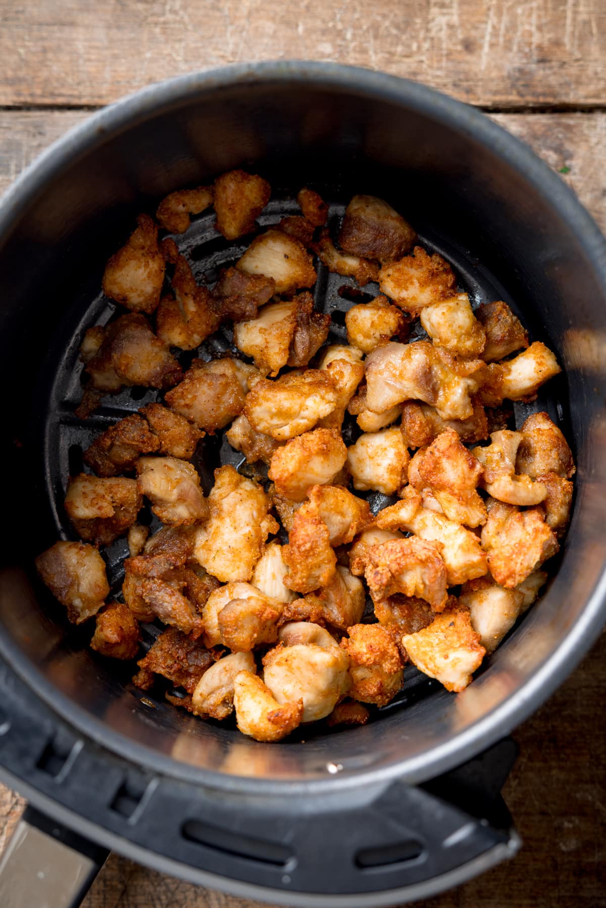 Overhead image of crispy air fryer chicken pieces in an air fryer basket. The basket is on a wooden background.