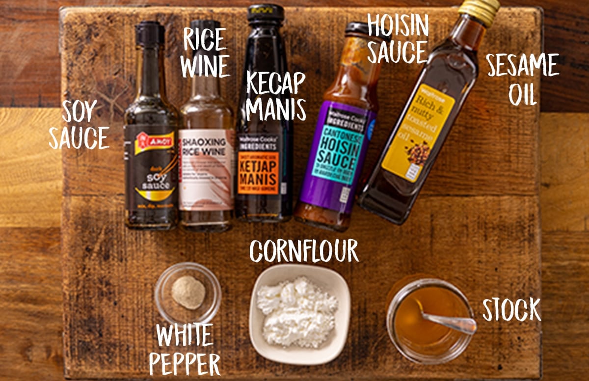 Ingredients for mushroom chow mein sauce are laid out on a wooden board. The ingredients are labelled in white text.