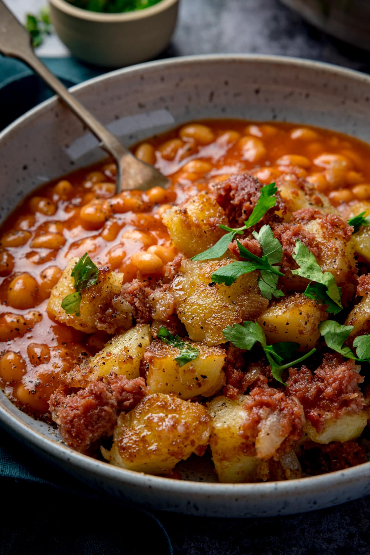 Tall image of corned beef hash with beans in a light bowl with parsley on top. There is a fork sticking out of the beans.