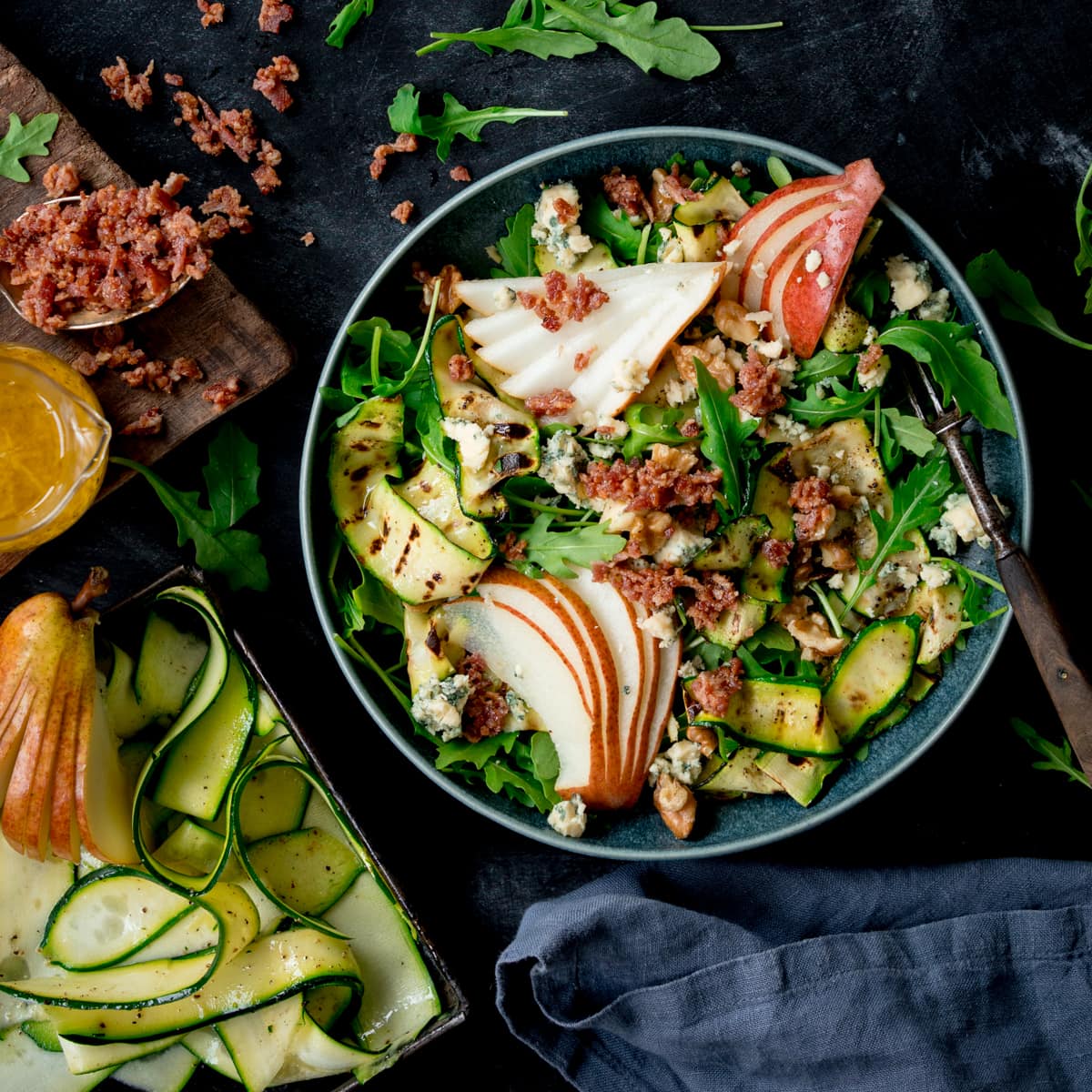 Overhead picture of a grilled courgette, bacon and pear salad in a blue bowl.
