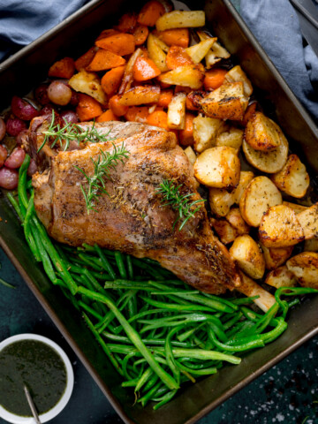 Overhead picture of a large roasting pan with a roast leg of lamb with veggies and potatoes in there too.
