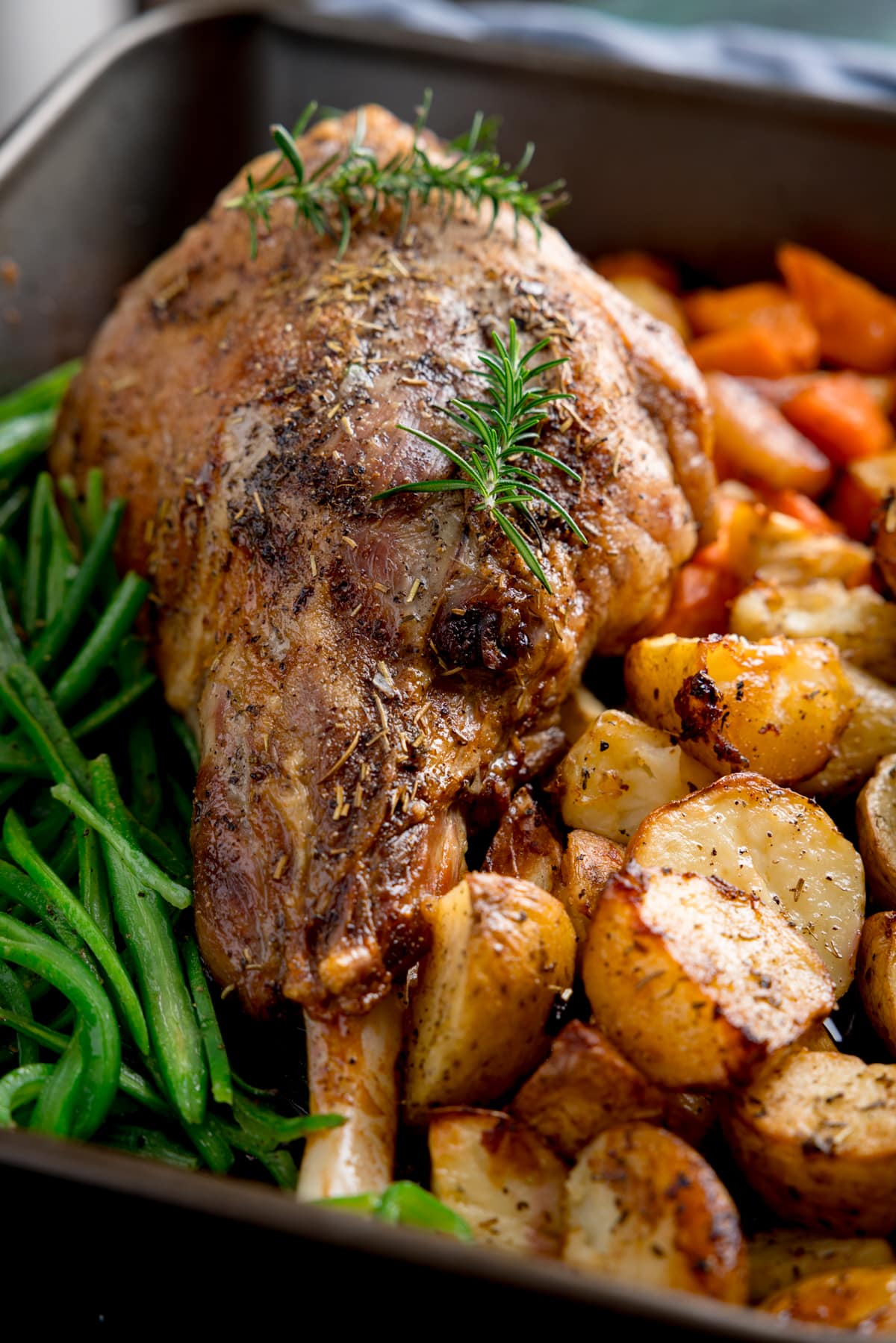 Close up picture showing a roast lego of lamb with nice shiny and crispy texture to the outside with veggies also in the pan but slightly out of focus.