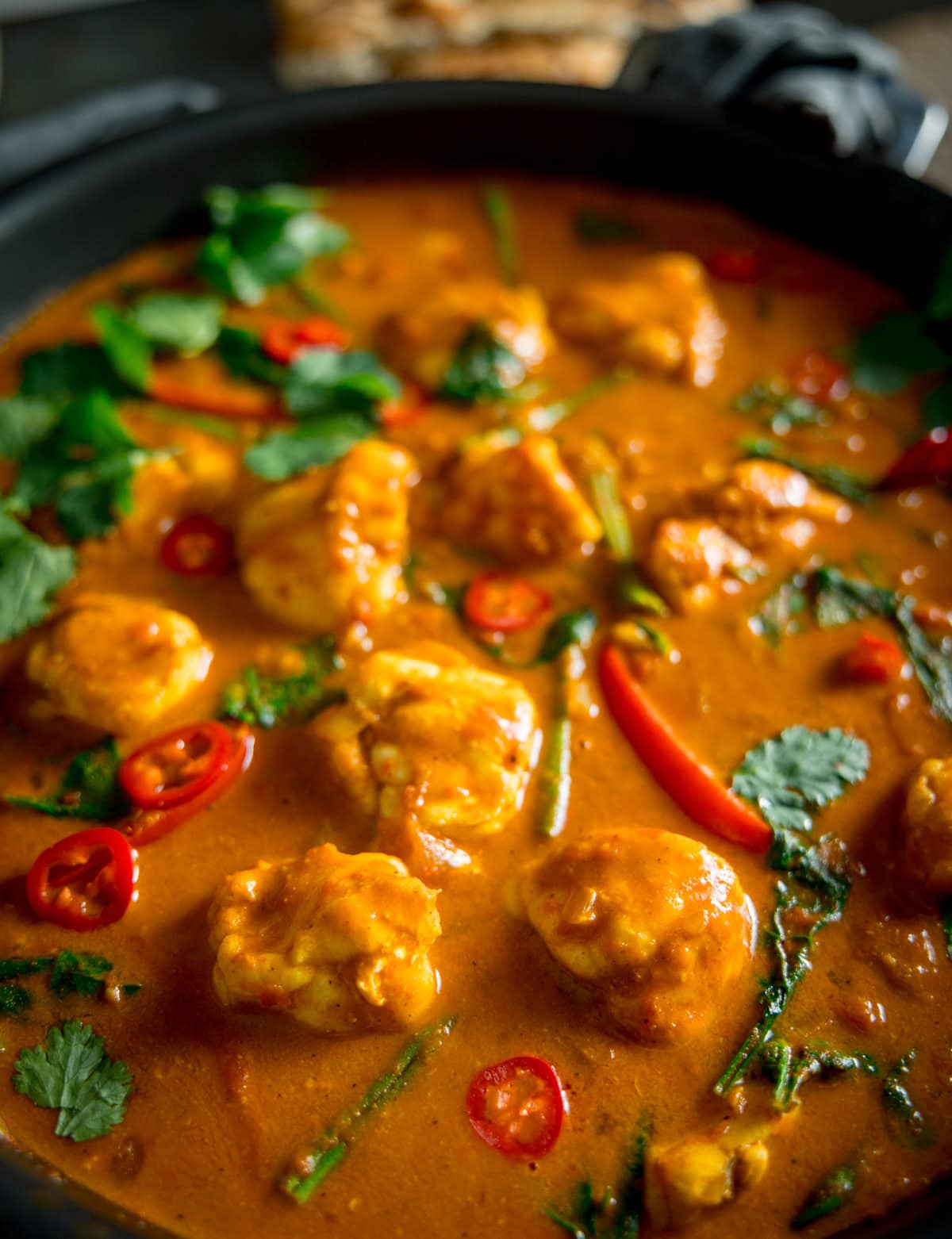 A closeup shot of Monkfish Coconut Curry in a grey pan, topped with coriander. On a grey surface with a grey napkin in the background.