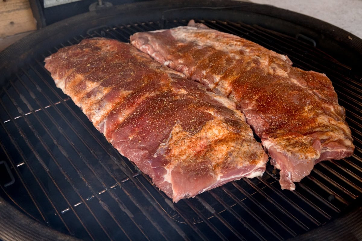 A prep shot of BBQ Dry Rub Ribs. There are two racks of seasoned ribs laid out on a black barbeque, which is heated to 120 degrees Celsius.
