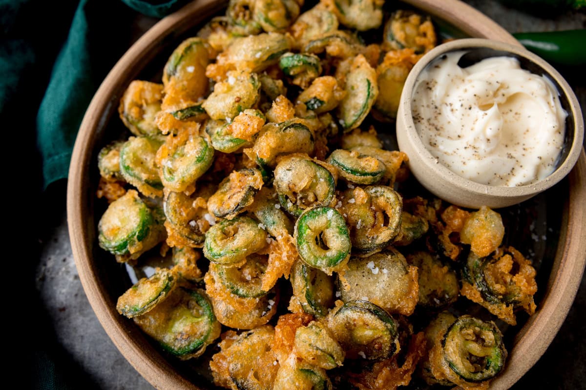 Slices of crispy battered jalapeños in a bowl with a mayonnaise dip.