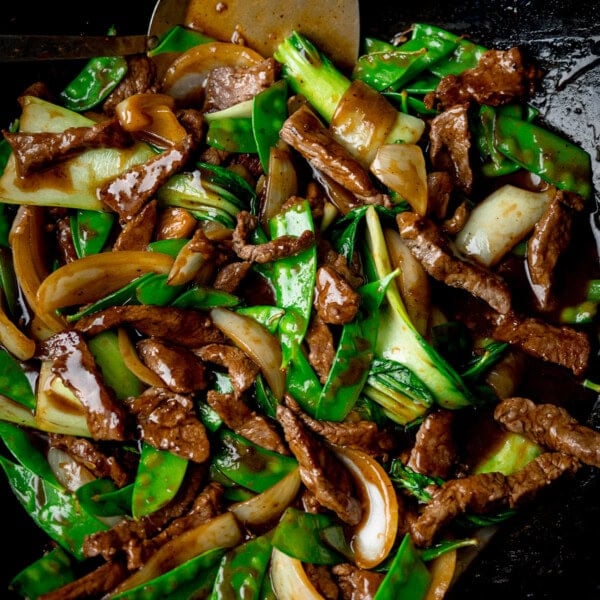 Stir-fried beef with mangetout, onions, and pak choi in a glossy hoisin beef stir-fry sauce, served in a pan with a metal spatula.