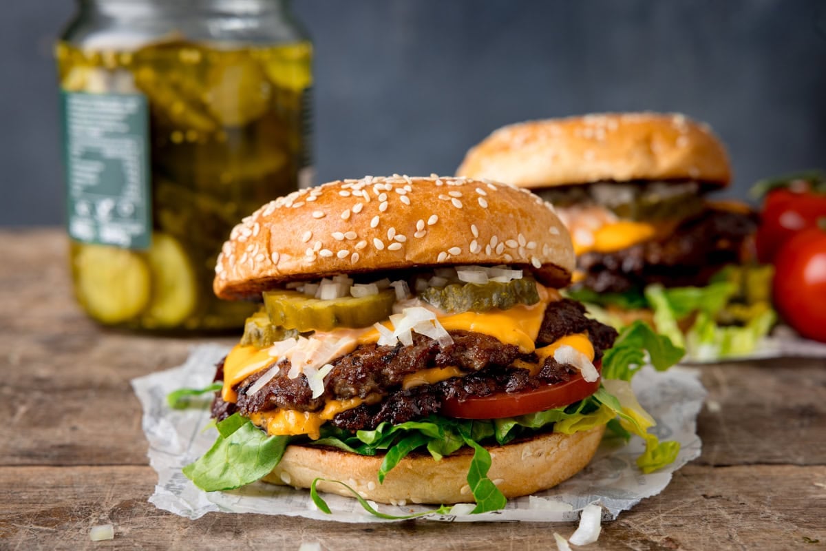 Double cheeseburger with lettuce, tomato, and pickle in a sesame seed bun.
