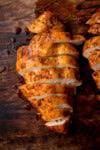A tall, overhead image of Air Fryer Chicken Breast. There are two, cooked chicken breasts next to each other. One of the chicken breasts is placed in the centre of the image, and the other is slightly to the right, so it is only partially seen. The chicken breasts are cut into horizontal strips. This is all set on a dark, wooden background.