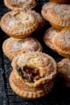 A close up picture of a frangipane mince pie with a bite taken out of it. The picture is highlighting the textures of the crumble shortcrust pastry, the mincemeat and the chewy frangipane topping.