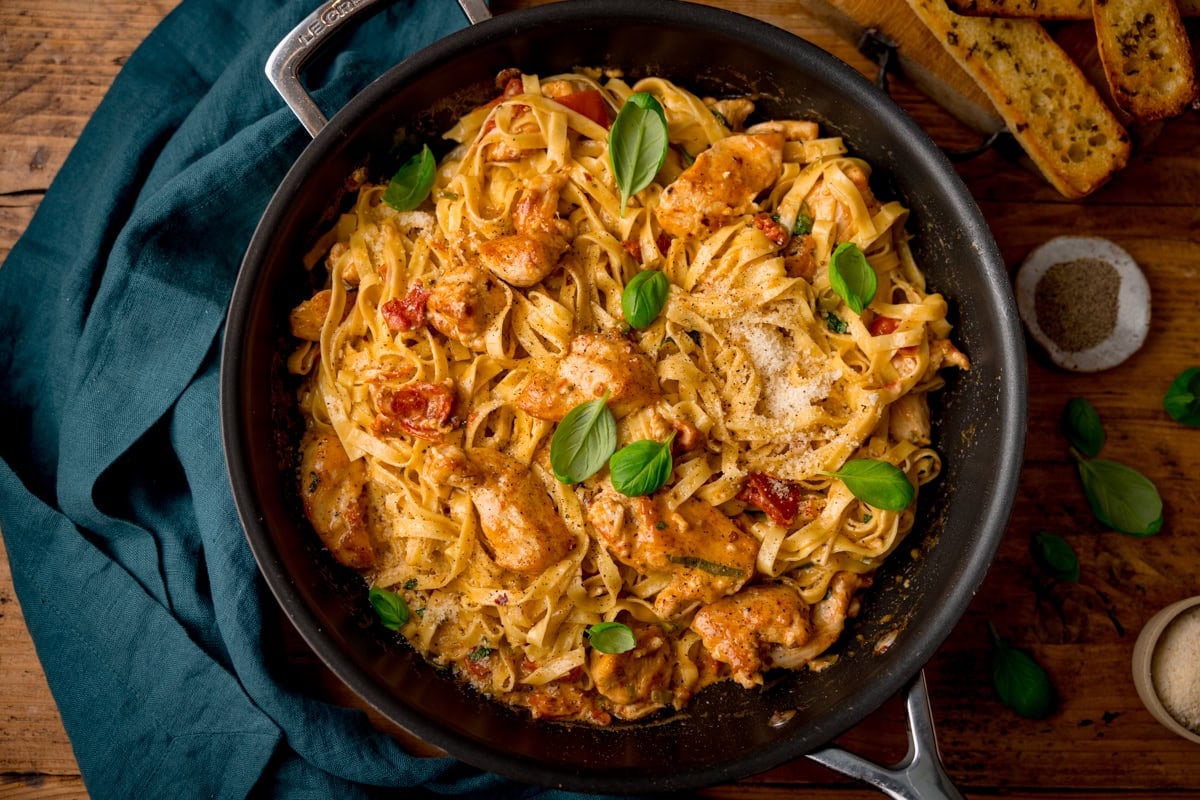 A pan of tagliatelle in a creamy sauce with diced chicken and sun dried tomatoes and parmesan.