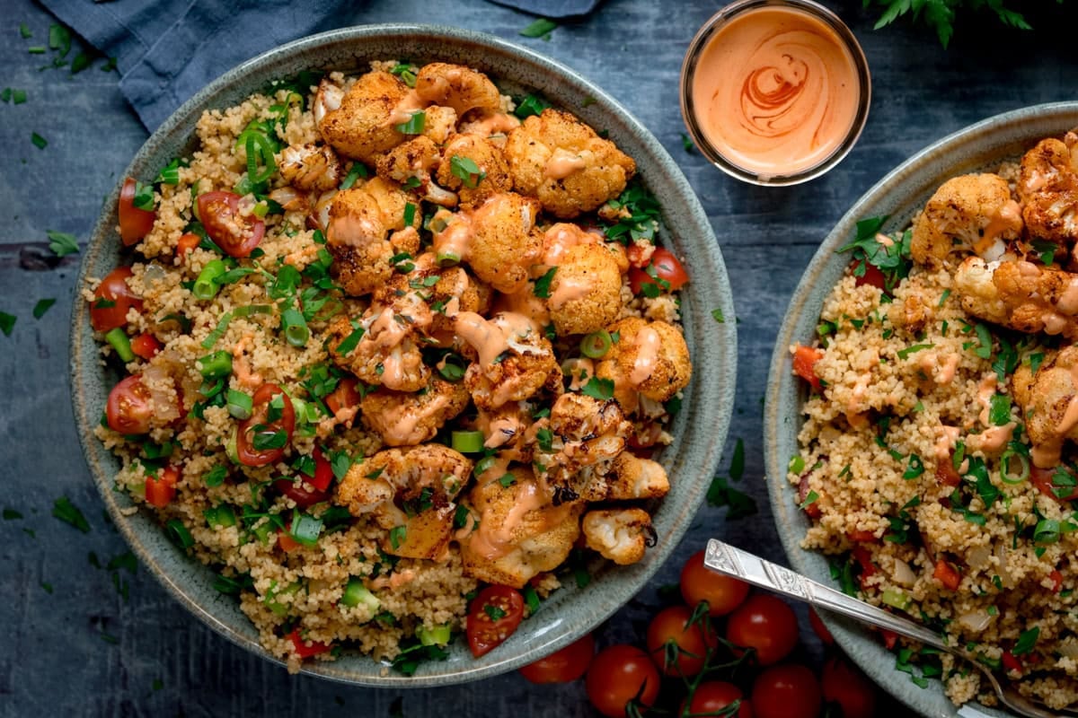 A bowl of roasted cauliflower florets with tomato and bell pepper couscous drizzled with spicy  mayo