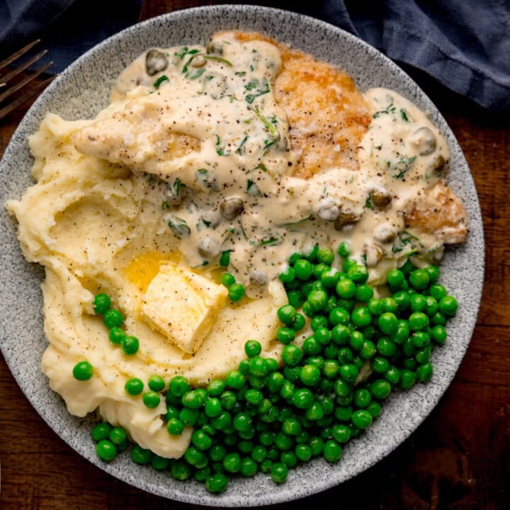 Plate with lemon butter sea bream in creamy sauce, mashed potatoes with butter, and green peas on a grey dish.
