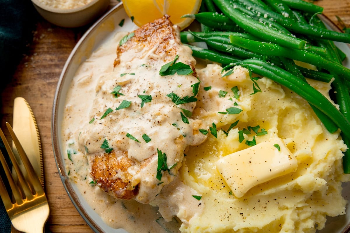 Chicken breast with a creamy sauce on top served with mashed potatoes and green beans.