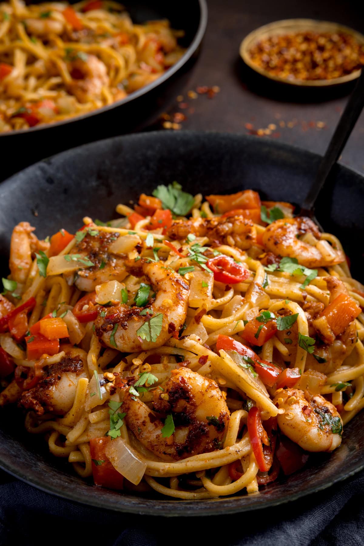 A black bowl filled with Cajun prawn noodle stir-fry, mixed with peppers, onions, and garnished with chopped coriander.