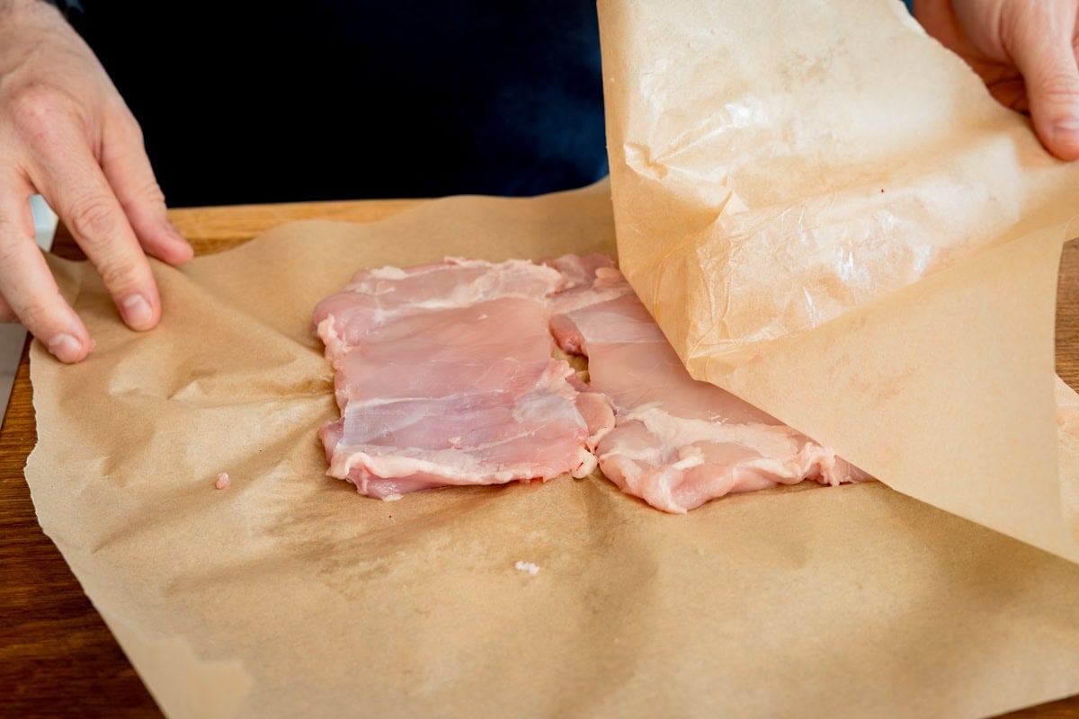 Raw chicken thighs for a Chicken Döner recipe being covered with baking paper on a wooden surface.