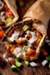 A flatbread wrap filled with grilled chicken doner recipe meat, diced cucumber, onions, tomatoes, and a drizzle of garlic sauce, served on a wooden board.