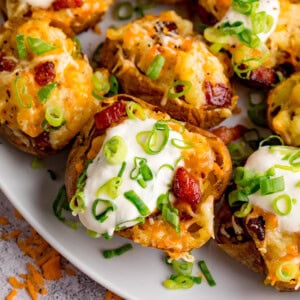 A plate of cheese and bacon potato skins topped with soured cream, melted cheese, crispy bacon pieces, and sliced spring onions.