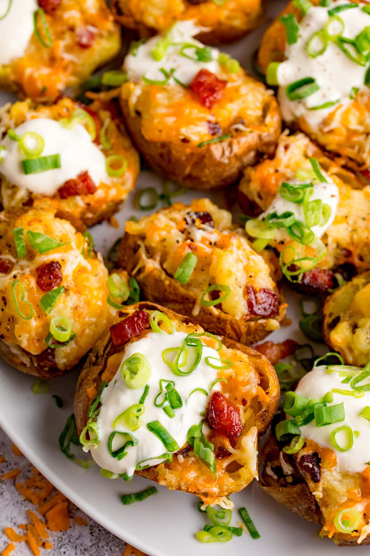 Loaded Potato Skins: Baked potato halves topped with melted cheese, soured cream, bacon pieces, and chopped spring onions arranged on a white plate.