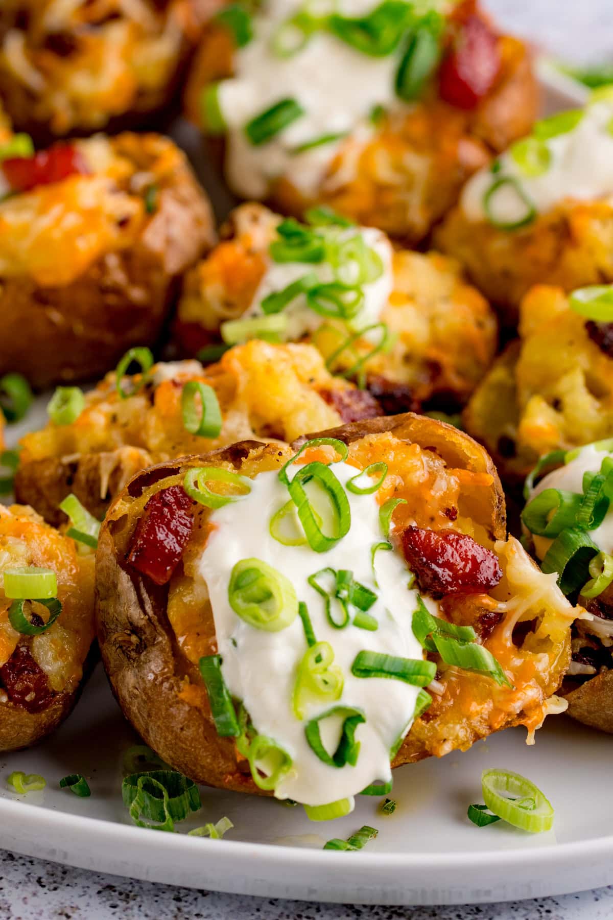 Baked cheese and bacon potato skins topped with soured cream and chopped spring onions, served on a white plate.