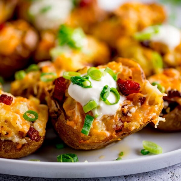 A plate of Loaded Potato Skins topped with melted cheese, soured cream, bacon pieces, and sliced spring onions.