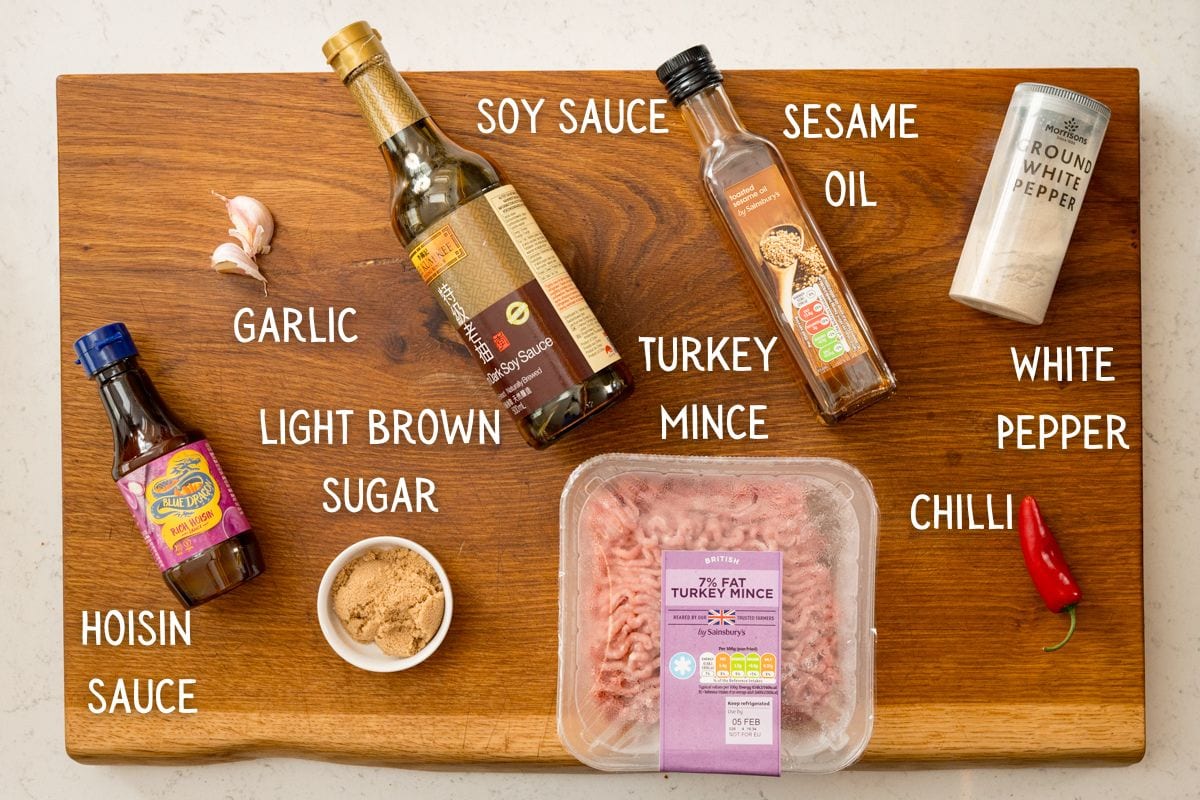 A wooden board holds turkey mince for turkey lettuce wraps, soy sauce, hoisin sauce, light brown sugar, garlic, sesame oil, white pepper, and a red chilli, each labelled with text.
