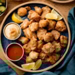 A plate of Air Fryer Chicken Karaage bites served with lemon wedges, mayonnaise, and red dipping sauce on a blue plate.