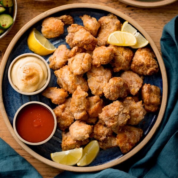 A plate of Air Fryer Chicken Karaage bites served with lemon wedges, mayonnaise, and red dipping sauce on a blue plate.