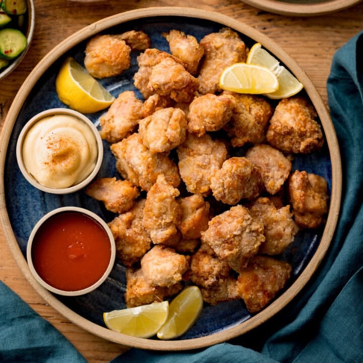 A plate of Air Fryer Chicken Karaage bites served with lemon wedges, mayonnaise, and red dipping sauce on a blue plate.